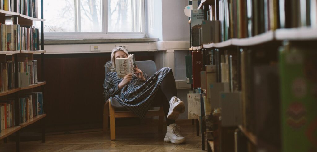 Frau liest in einem Stuhl in einer Bücherei ein Buch.